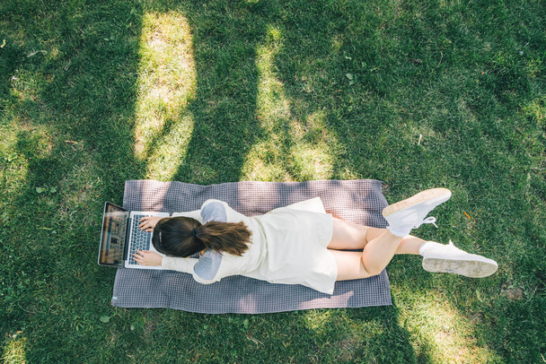 mujer bonita joven acostada sobre una manta de hierba verde con ordenador portátil. vista aérea
 - Foto, Imagen