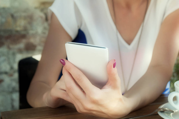 Γυναικεία χέρια με μωβ μανικιούρ χρησιμοποιώντας λευκό smartphone στο καφενείο, γκρο πλαν  - Φωτογραφία, εικόνα