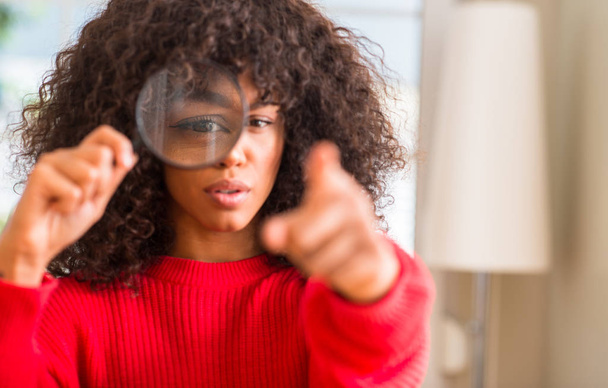 Zvědavý afroamerické ženy při pohledu skrz zvětšovací sklo ukazující prstem na kameru a na vás, rukou znamení, pozitivní a sebevědomý gesto z přední - Fotografie, Obrázek