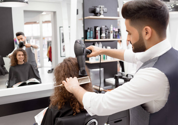 Backview of hairstyler doing hairdress for smiling curly female client. - Valokuva, kuva