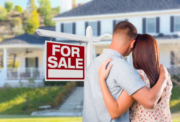 Military Couple Looking At House with For Sale Real Estate Sign In Front. - 写真・画像