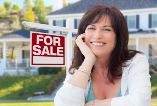 Frau mittleren Alters vor Haus mit zu verkaufendem Immobilienschild im Hof. - Foto, Bild