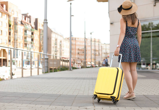 Young woman with yellow carry on suitcase outdoors - Foto, afbeelding