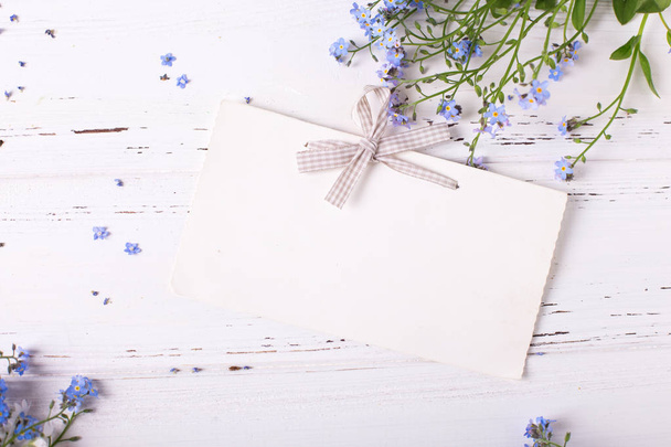 Empty tag and frame from blue forget-me-nots or myosotis flowers on white wooden background - Photo, Image