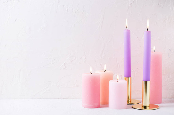 Pink and violet color burning candles near by white textured wall - Foto, imagen