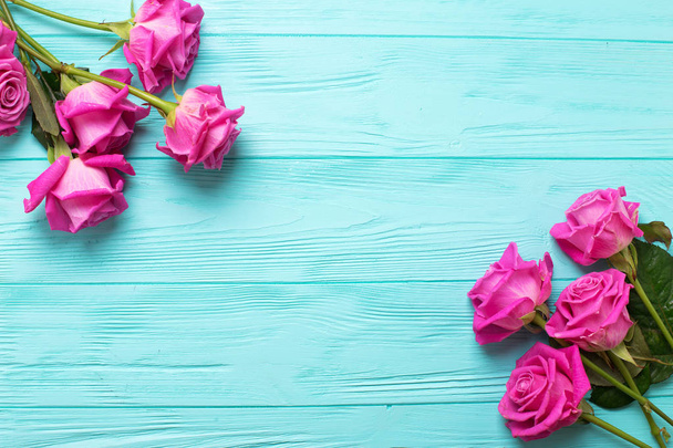 Border from pink roses flowers on teal color wooden background - Фото, изображение