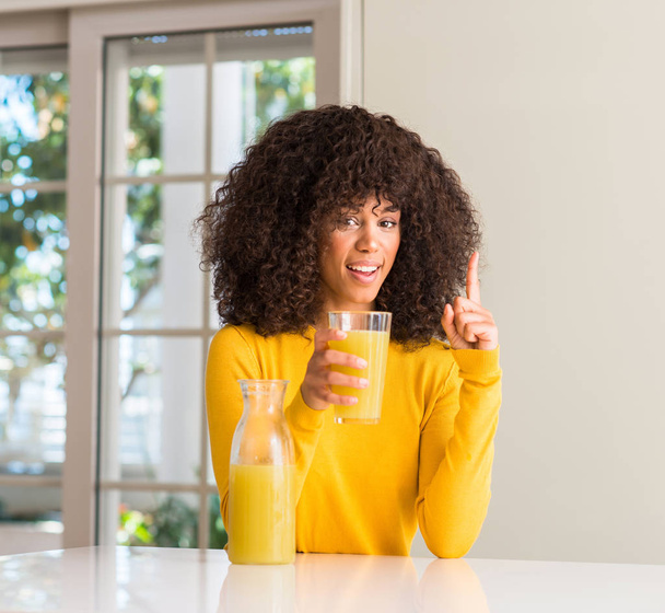 Afrikai-amerikai nő, egészséges gyümölcslé otthon iszik meglepett mutatóujjal egy ötletet vagy kérdést boldog arc, az első - Fotó, kép