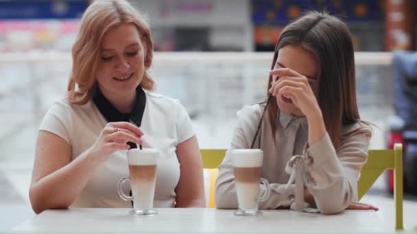 Deux jeunes femmes parlent et boivent du café assis dans un café. - Séquence, vidéo