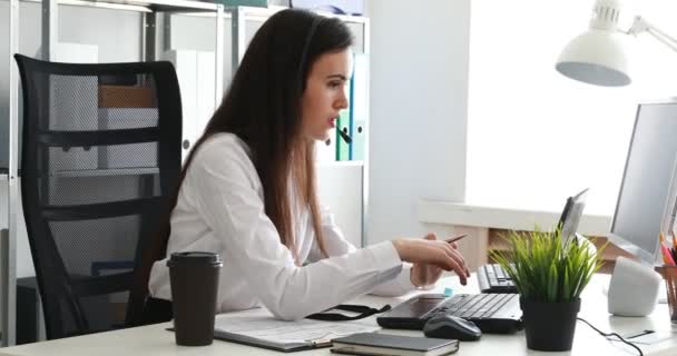 woman speaking on headset and using laptop in modern office - Felvétel, videó