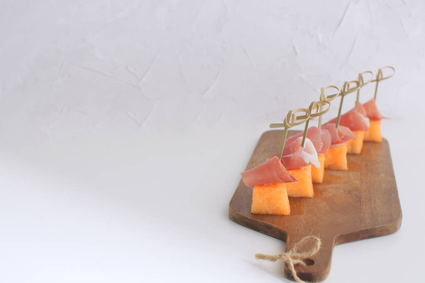 Диня з Канапе prociutto на шпажки Melong з хамон на дерев'яні обробні дошки ресторан для гурманів блюдо традиційні італійські іспанські закуски тапас білий фон копію простір - Фото, зображення