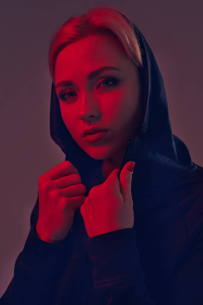 Young pretty woman wearing a black hood and shorts on dark background. Portrait - Foto, imagen