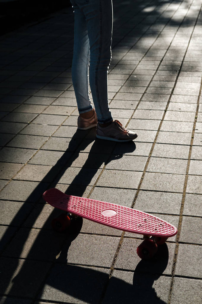 Gros plan du skateboard rose et des jambes féminines en baskets dans la rue au lever du soleil. Adolescente fille avec penny skateboard
 - Photo, image