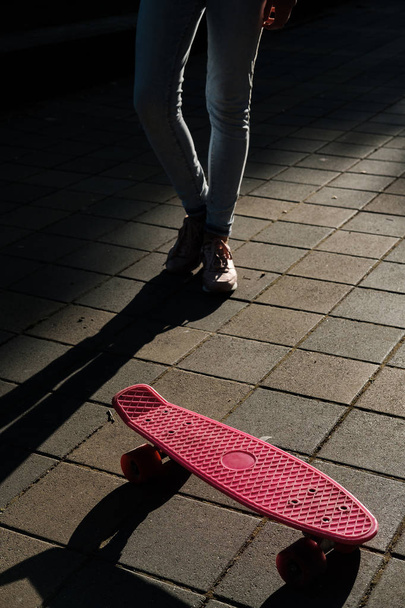 Primer plano de patineta rosa y piernas femeninas en zapatillas de deporte en la calle al amanecer. Adolescente chica con penny monopatín
 - Foto, imagen