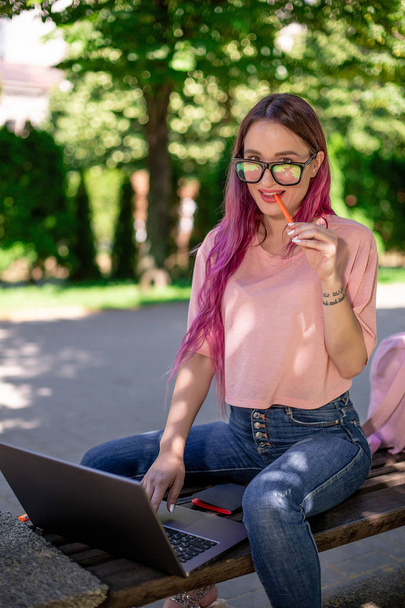 Chica joven está estudiando en el parque de primavera, sentado en el banco de madera y la navegación en su ordenador portátil
 - Foto, imagen