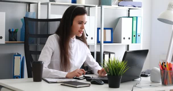 γυναίκα μιλώντας στο ακουστικό και να χρησιμοποιούν φορητό υπολογιστή στο σύγχρονο γραφείο - Πλάνα, βίντεο