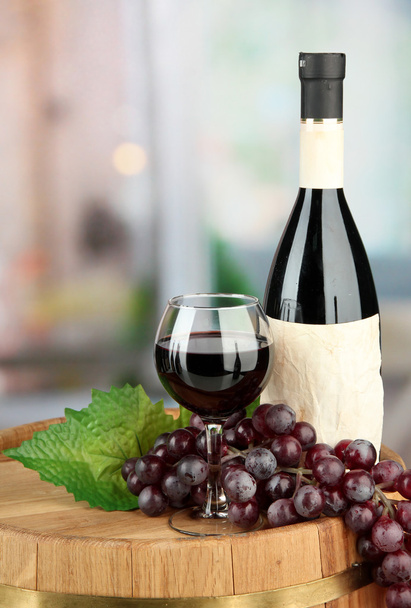 Composition of wine bottle, glass and grape,on wooden barrel, on bright background - Fotó, kép
