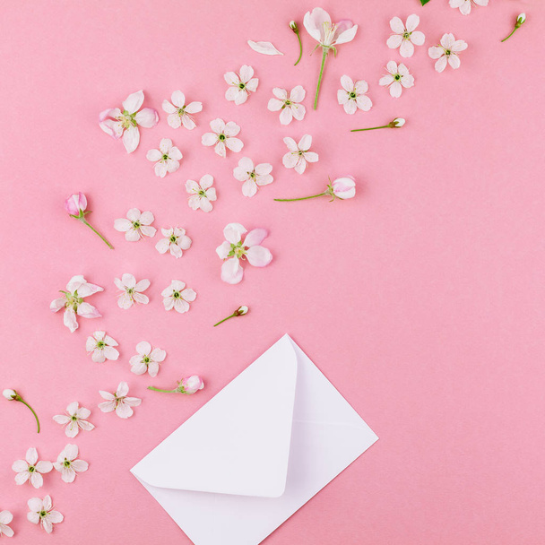 Square flat lay concept top view of blank letter envelope and spring cherry tree flowers on millennial pink background with copy space in minimal style, template for celebration, valentine cards - Фото, зображення