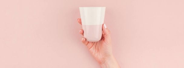 Banner largo y ancho de la mano de la mujer sosteniendo la taza de café con espacio de copia sobre fondo rosado milenario en estilo minimalista. Plantilla conceptual para blog femenino, redes sociales
 - Foto, imagen