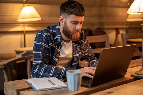 Jungprofi surft im Internet auf seinem Laptop in einem Café - Foto, Bild