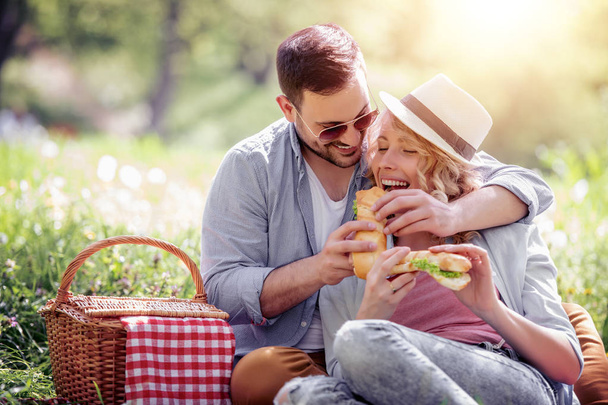 Счастливая молодая пара ест бутерброды на открытом воздухе
. - Фото, изображение