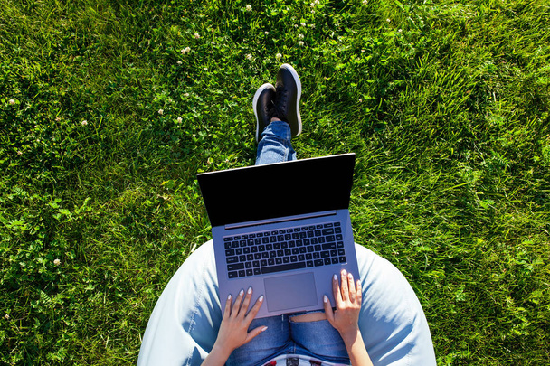 Top view. Woman working on laptop pc computer with blank black empty screen to copy space in park on green grass sunshine lawn outdoors. - Foto, imagen