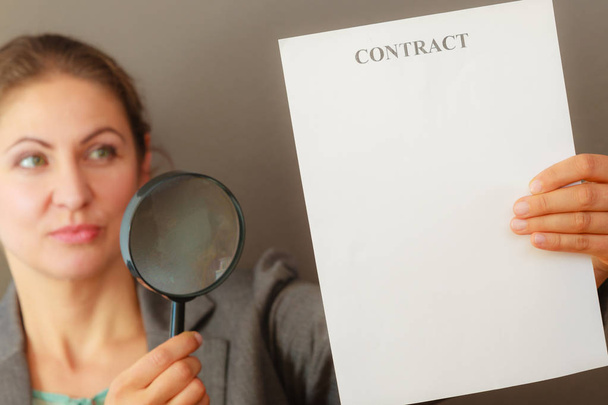 Contracts and agreements concept. Adult beauty woman in jacket holding showing contract. Close up portrait of person with loupe studying agreement. - Foto, Imagen