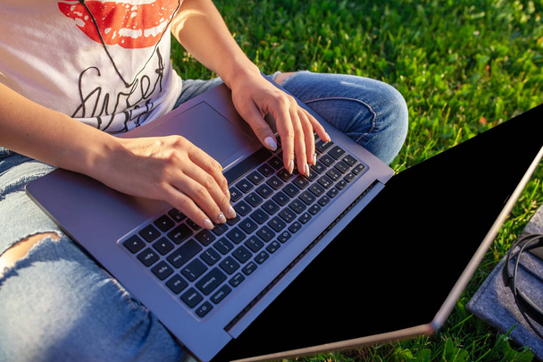 Zbliżenie dłoni na klawiaturze. Kobieta pracuje na komputerze pc laptop z pusty czarny ekran pusty skopiować miejsca w parku na zielonej trawie słońce trawnik na zewnątrz. Mobilne biuro. Koncepcja działalności freelancerskiej - Zdjęcie, obraz