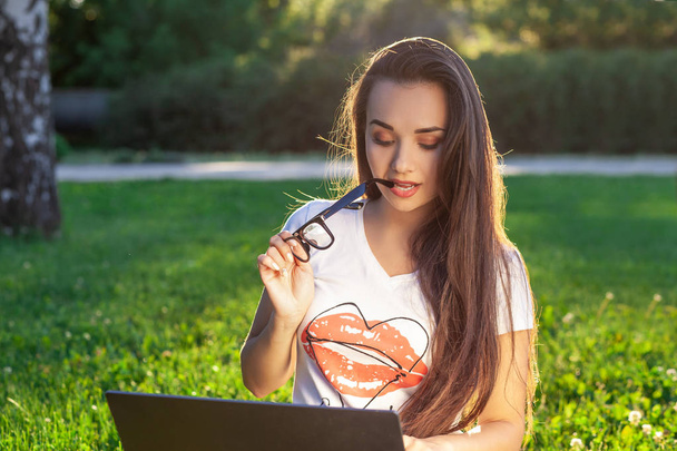 若い女性が公園で緑の草にコンピューターを使用して。学習教育またはフリーランスの屋外作業やリラクゼーション コンセプト アイデア背景。太陽フレア - 写真・画像