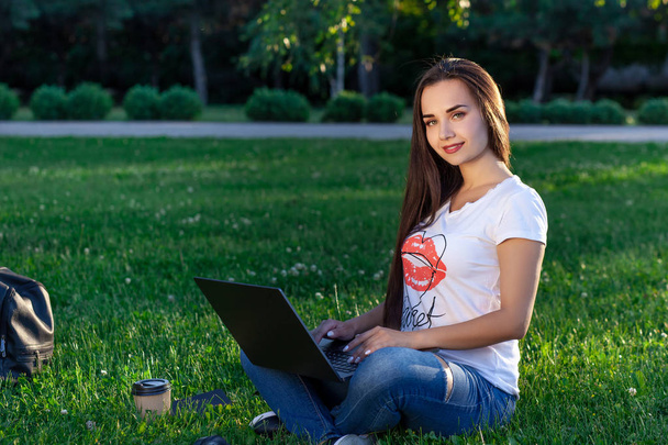 Fiatal nő segítségével a számítógép a zöld gyep a parkban. Oktatás-tanulás vagy szabadúszó munka szabadtéri vagy relaxációs koncepció ötlet háttér. - Fotó, kép