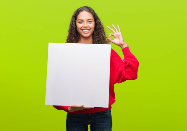 Young hispanic woman holding blank banner doing ok sign with fingers, excellent symbol - Photo, Image