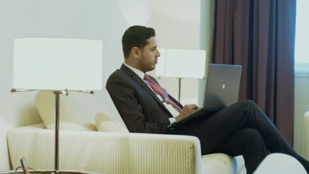 Pohledný podnikatel hispánské pracuje na svůj přenosný počítač v hotelovém pokoji, mluvit s někým, příprava na obchodní jednání technologie komunikační úspěch podnikatel důvěru koncept - Záběry, video