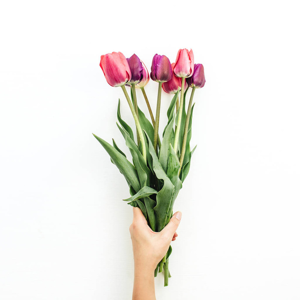 Woman hand holding tulips bouquet on white. Flat lay, top view flowers festive background. - Photo, Image