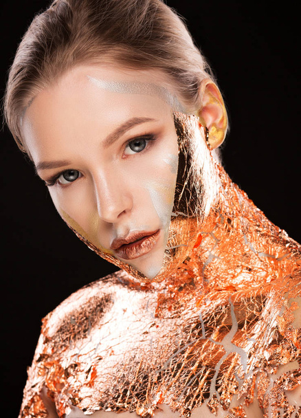 Красочный снимок модной блондинки с креативным макияжем и золотой фольгой на плечах и лице
 - Фото, изображение