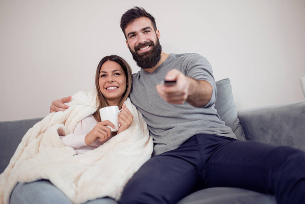 Happy couple watching television, drink coffee and eat popcorn on the couch - family, recreation, fun and happiness concept. - Foto, afbeelding