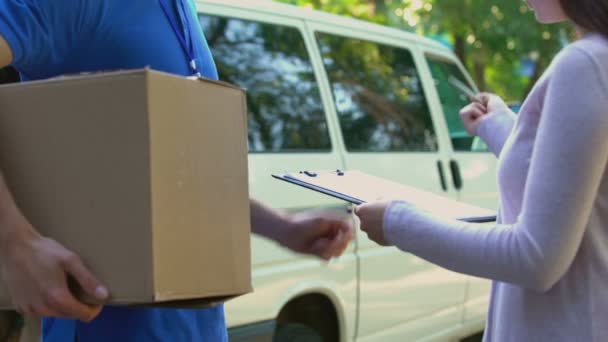 Woman signing form and receiving cardboard parcel, delivery company distribution - Imágenes, Vídeo