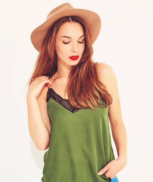 Young stylish girl model in casual summer green clothes and brown hat with red lips, posing near white wall - Foto, Imagen