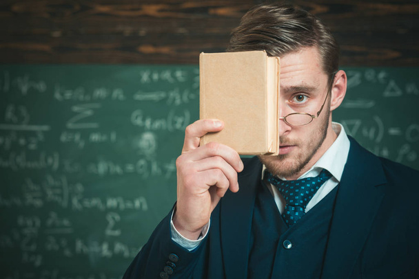 You should remember. Teacher formal wear and glasses looks smart, chalkboard background. Man unshaven holds book in front of face. Teacher insists on need to memorize information. Education concept - Photo, image
