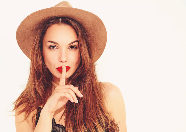 Young stylish girl model in casual summer green clothes and brown hat with red lips showing silence gesture with finger, isolated  - Photo, Image