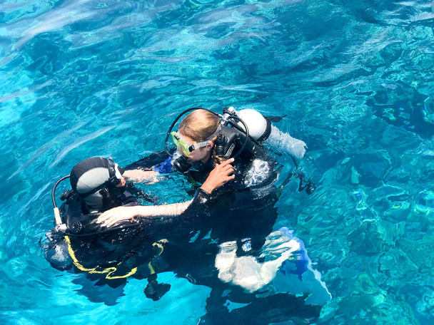 Kaksi sukeltajaa mustissa sukelluspuvuissa, mies ja nainen happipullojen kanssa uppoavat läpinäkyvän sinisen veden alla meressä, valtameri trooppisessa paratiisissa lämpimässä lomakeskuksessa
. - Valokuva, kuva