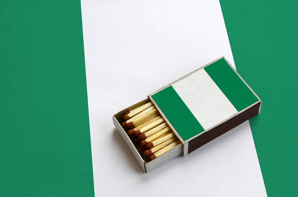 Bandera de Nigeria se muestra en una caja de fósforos abierta, que está llena de partidos y se encuentra en una gran bandera
. - Foto, Imagen