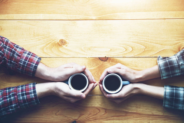 Hands of couple with two cups of coffee on wooden table, elevated view - Фото, изображение