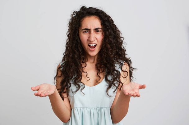 Portret van boos boos jonge vrouw met lang donker krullend haar en geopende mond schreeuwen en copyspace op beide palmen geïsoleerd op een witte achtergrond te houden voelt geïrriteerd - Foto, afbeelding