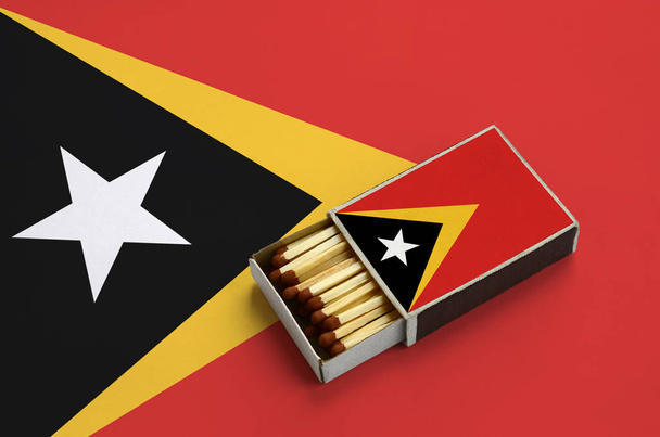 Bandeira de Timor Leste é mostrada em uma caixa de fósforos aberta, que é preenchida com fósforos e fica em uma grande bandeira
. - Foto, Imagem