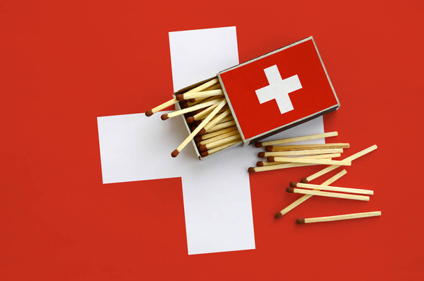 Switzerland flag  is shown on an open matchbox, from which several matches fall and lies on a large flag. - Foto, immagini