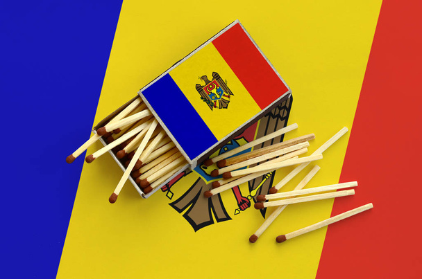 Le drapeau moldave est représenté sur une boîte d'allumettes ouverte, dont plusieurs allumettes tombent et reposent sur un grand drapeau
. - Photo, image