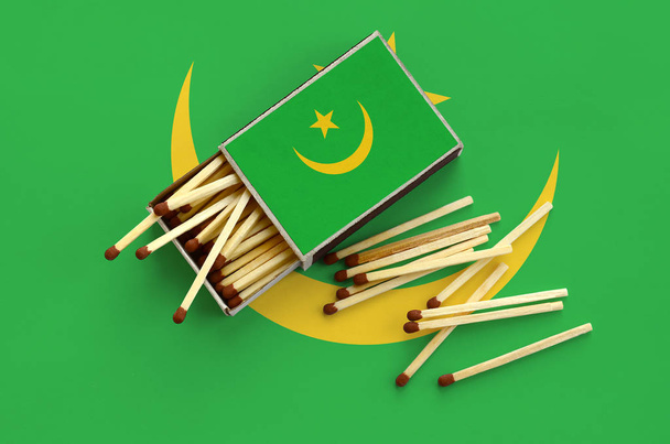 Bandiera Mauritania è mostrato su una scatola di fiammiferi aperta, da cui cadono diverse partite e giace su una grande bandiera
. - Foto, immagini