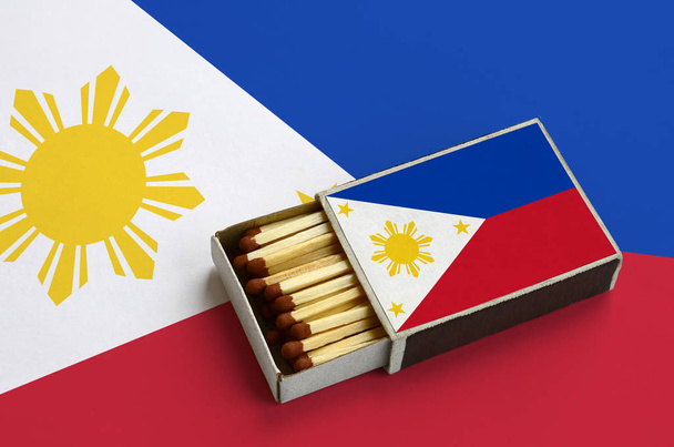 Le drapeau des Philippines est affiché dans une boîte d'allumettes ouverte, remplie d'allumettes et reposant sur un grand drapeau
. - Photo, image