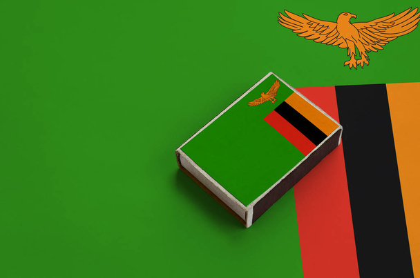 La bandiera dello Zambia è raffigurata su una scatola di fiammiferi che giace su una grande bandiera
. - Foto, immagini