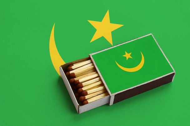 Le drapeau mauritanien est montré dans une boîte d'allumettes ouverte, remplie d'allumettes et posée sur un grand drapeau
. - Photo, image