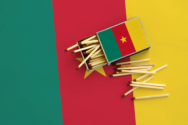 Drapeau du Cameroun est représenté sur une boîte d'allumettes ouverte, dont plusieurs matchs tombent et se trouve sur un grand drapeau
. - Photo, image